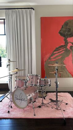 a drum set sitting on top of a pink rug in front of a large painting