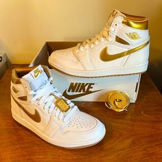 Air Jordan 1 High Og In All White With Glossy Gold Accents, Gold Swoosh, And A Gold Nike Air Keychain! Premium Leather, Padded Ankle Collar, Rubber Outsole. Clean Look With A Bit Of Glam. Nwt Comes In Nike Box Without Lid, And An Extra Set Of Gold Laces. Nhn4sa7x1t6e White And Gold Nike Shoes, Gold Jordans, Gold Nike Shoes, Shoes Nike Women, Air Jordan 1 White, White And Gold Shoes, Jordan 1 Outfit Women, Nike Box, Gold Nike