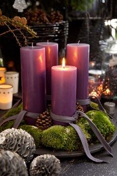 three candles are sitting on a plate with moss and pine cones