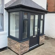 a small brick building with a black roof and glass windows on the side of it