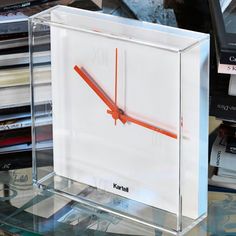 a glass clock sitting on top of a table next to stacks of books and magazines