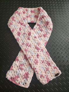 a pink and white knitted scarf laying on top of a black table next to a cell phone