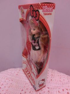 a small doll in a box on a pink tablecloth with a hello kitty design