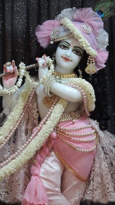 the statue is dressed in pink and white with pearls on it's head, holding a flute