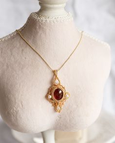 An artisan-made 14K gold-filled pendant, with a Garnet cabochon and faced cubic, is carefully hung from ball chain with a lobster clasp. This captivating pendant, boasting artwork of incomparable skill and a magnificent combination of red Garnet with an orange hue and translucent red Cubic, offers a perfect juxtaposition of poise and dynamism, making it an elitist piece of jewelry. The length of necklaces is approx. 24". Follow me on Instagram: @cubic_jewels Gold Cabochon Teardrop Pendant Jewelry, Gold Cabochon Teardrop Pendant, Antique Cabochon Round Pendant Necklace, Yellow Gold Cabochon Teardrop Pendant Necklace, Victorian Pendant Necklace With Cabochon, Victorian Cabochon Pendant Necklace, Gold Pendant Necklace With Cabochon, Pendant Amulet Necklace With Cabochon, Gold Cabochon Pendant Necklace