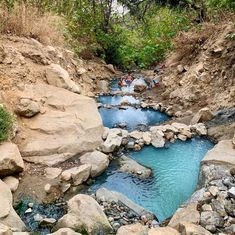 people are swimming in the blue water near some rocks