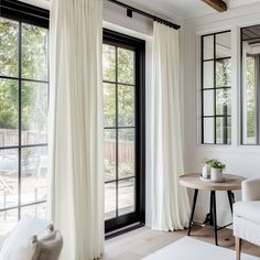 a living room filled with furniture and large windows covered in white drapes next to a small table