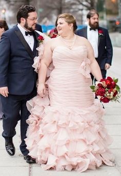 a man and woman in formal wear walking down the street with red flowers on their bouquets