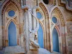 a stone statue in front of a building with arched windows and an elaborate gargoyle