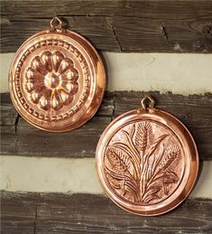 two copper medallions sitting on top of a wooden table next to each other and one has a flower in the center