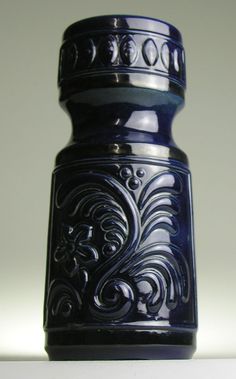 a blue vase sitting on top of a white table next to a black object in the background