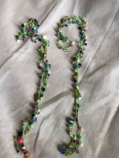 a long necklace with beads is laying on a bed next to a white sheet that has the letter o written in it