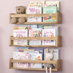 three wooden bookshelves with children's books on them against a pink wall