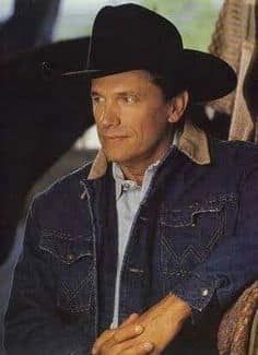 a man wearing a black cowboy hat sitting in a chair with his hand on his hip