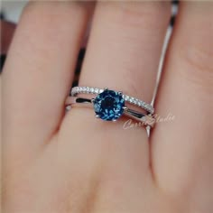 a close up of a person's hand holding a ring with a blue stone