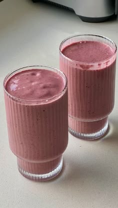 two glasses filled with pink smoothie sitting on top of a counter