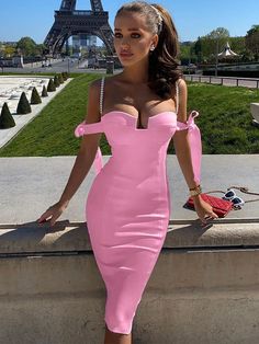 a woman in a pink dress leaning against a wall with the eiffel tower in the background