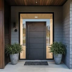 two large planters are on the side of a gray door with an entrance mat