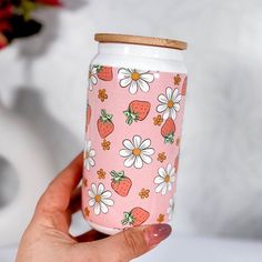 a hand holding a pink cup with strawberries and daisies on it