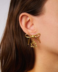 A Mensch is a very elegant person and my oh my if these earrings aren't the most elegant! Our lovely hand crafted bronze bow with a twinkling jewish star below. How Menschy! Sold as a pair. Drop: 1" All jewelry is made by hand to order. Jewelry will ship 2-3 weeks from the order date (if not sooner!) Yellow Gold Earrings With Dangling Charms As Gift, Yellow Gold Earrings With Dangling Charms For Gift, Formal Pendant Earrings, Elegant Clip-on Dangle Flower Earrings, Elegant Dangle Clip-on Flower Earrings, Formal Single Pendant Earring, Gold Sterling Silver Clip-on Earrings For Party, Classic Brass Jewelry For Party, Yellow Gold Bridal Earrings For Gift