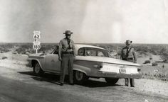 two men standing next to an old car in the desert