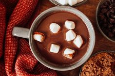 hot chocolate with marshmallows in a mug surrounded by other ingredients on a wooden table