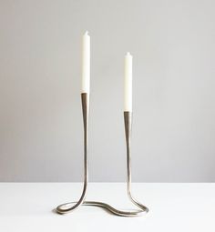 two silver candles sitting next to each other on top of a white table with one candle in the middle