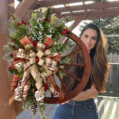 a woman is holding a christmas wreath on a wagon wheel