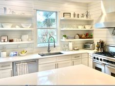 a kitchen with white cabinets and open shelvings on the wall above the stove