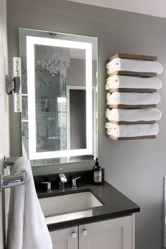 a bathroom sink with towels hanging on the wall and a mirror above it that has lights