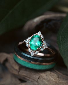 two wedding bands with an emerald and diamond ring on top of each other next to a leaf