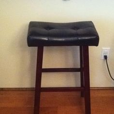 a black leather stool sitting in front of a wall with a clock on it's side