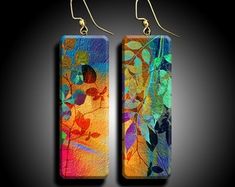 pair of earrings with colorful leaves on them, hanging from hooks against a black background