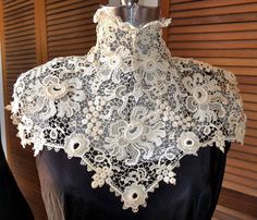 a black dress with white lace on it and a mannequin in the background