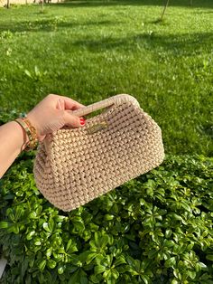 a hand holding a straw purse in front of green grass and bushes on a sunny day