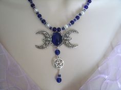 "This beautiful necklace has a cobalt blue catseye set on a sterling silver plated triple moon pendant, a pewter silver pentacle, cobalt blue czech glass beads, pearl beads and pewter silver accent beads. 18\" long. Toggle clasp." Blue Gothic Metal Necklace, Gothic Blue Metal Jewelry, Blue Gothic Metal Jewelry, Gothic Blue Jewelry For Gifts, Blue Gothic Jewelry For Gifts, Blue Gothic Jewelry For Gift, Gothic Round Adjustable Necklace, Gothic Adjustable Round Necklace, Gothic Nickel-free Jewelry For Festivals