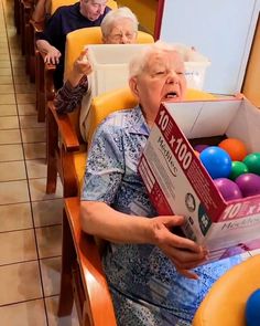 an elderly woman sitting in a chair holding a box with balls on top of it