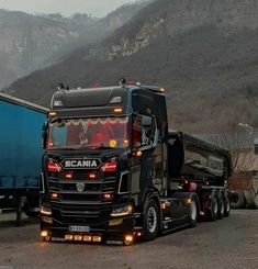 a black semi truck driving down a road next to a blue trailer and mountain range in the background