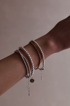 A hand with several bracelets rests against a neutral background. The bracelets are silver and gold with varying beads and chains, adding depth and texture to the wrist. Trendy Stackable Wrap Bracelet With Round Beads, Flexible Silver Stackable Bracelets, Silver Flexible Bracelet For Everyday Wear, Silver Flexible Bracelets For Everyday Wear, Trendy Silver Stretch Bracelet With Round Beads, Minimalist Stackable Bracelets With Round Beads, Stackable Round Bracelets, Flexible Stackable Silver Bracelets, Everyday Flexible Silver Bracelets