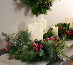 two candles are sitting on a table with evergreen, berries and pineconi wreaths