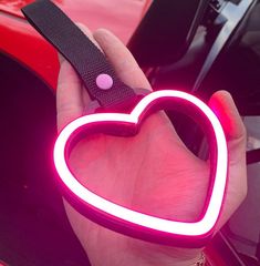 a person holding a neon heart shaped object in their left hand with the light on