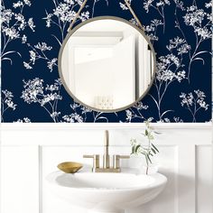 a mirror hanging on the side of a wall next to a sink and vase with flowers