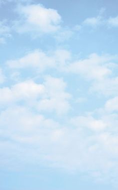 two people standing on the beach flying a kite in the blue sky with white clouds