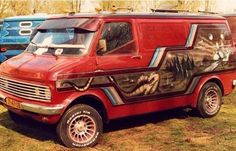 an old red van painted with images of animals on it's side, parked in the grass