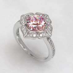 The Platinum Plated Sterling Silver Ring, Cushion Super Light Pink CZ Stone Milgrain Vintage 2 carat Engagement Ring, Pink Diamond Simulant Ring Cocktail Ring (Size 5 to 9) is nothing short of breathtaking. With its vintage-style vibe, it showcases an eye-catching light pink cushion cut cubic zirconia encircled by sparkling round cut accents set in milgrain edge finish petals being formed a heart shape. It would be a sensation at a garden party and a lovely complement to your little black dress Classic Pink Cluster Ring With Prong Setting, Classic Pink Cluster Ring With Center Stone, Pink Topaz Ring With Halo Setting As Gift, Pink Cubic Zirconia Halo Ring For Wedding, Fine Jewelry Flower Ring With Center Stone For Promise, Fine Jewelry Flower Ring With Center Stone, Classic Pink Cluster Ring With Halo Setting, Pink Topaz Promise Ring In Fine Jewelry Style, Pink Topaz Promise Ring With Prong Setting