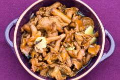 a bowl filled with meat and apples on top of a purple cloth covered tablecloth