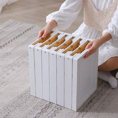 a girl in white dress playing with wooden blocks on carpeted floor next to rug