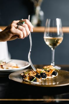 a person is eating food with a fork and glass of wine on the table in front of them