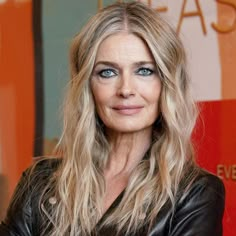 a woman with long blonde hair wearing a black leather jacket and smiling at the camera