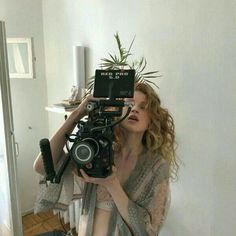 a woman holding a camera up to her face in front of a mirror with a potted plant on top of it